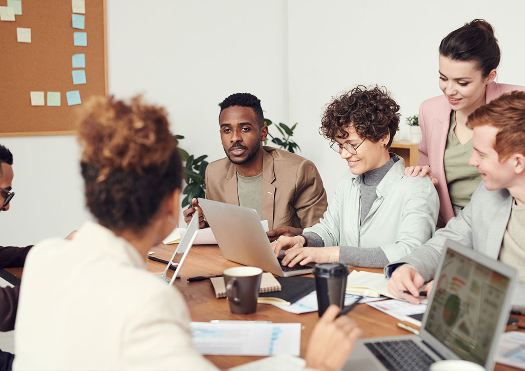 Lebendige und diverse Arbeitskultur und Austausch unter Mitarbeitenden am Tisch mit Laptops