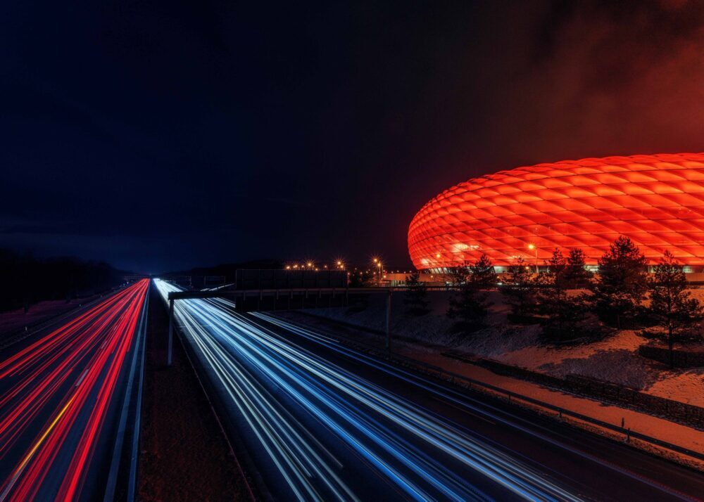 Autobahn im Großraum München mit rot erleuchteter Allianz Arena im Anschnitt